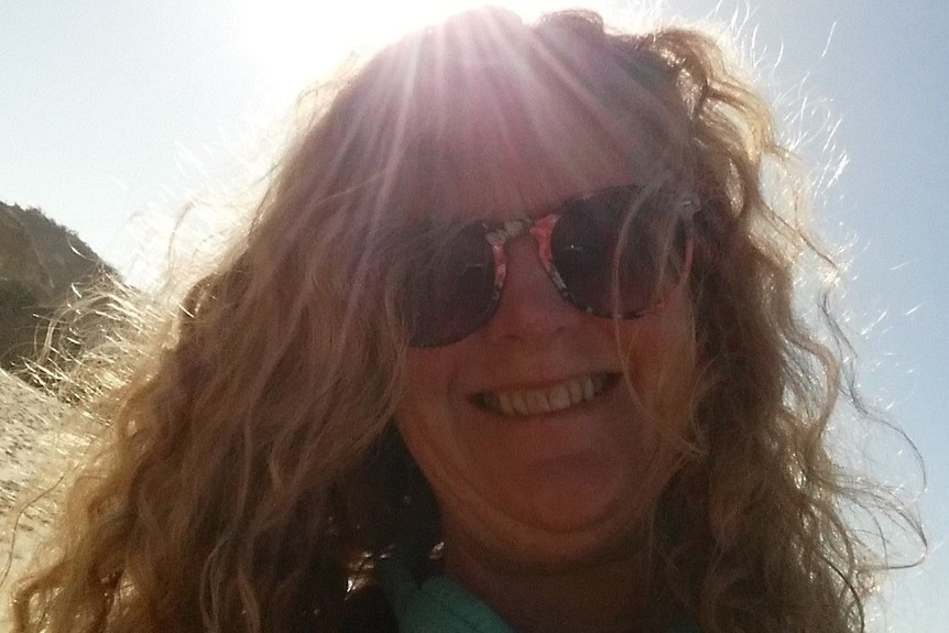 selfie of happy looking woman with curly hair smiling on beach with angelic lighting