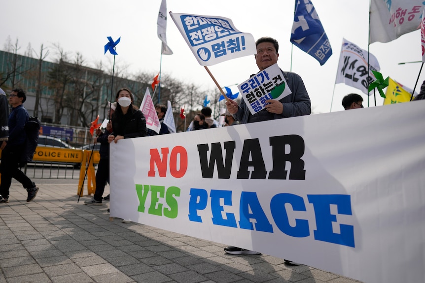 Protesters hold a large sign reading: "NO WAR YES PEACE."