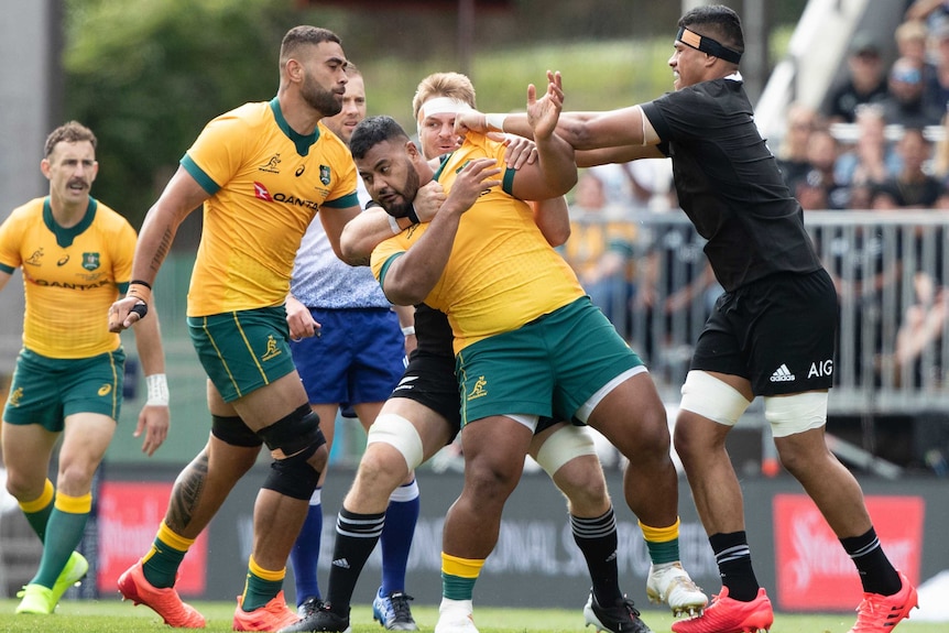 A New Zealand All Blacks players holds an Australian Wallabies opponent around the shoulders.