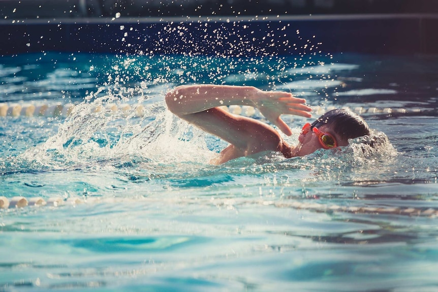 A boy swimming in a pool, with goggles on.