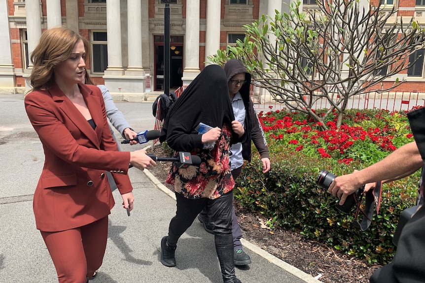 A woman covers her face as she leaves court flanked by reporters