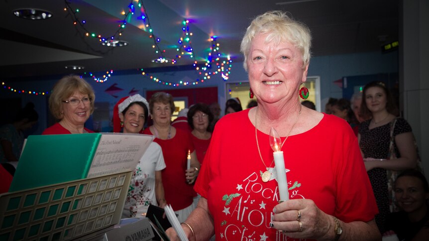 A woman leads Christmas carollers in a hospital ward.