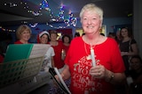 A woman leads Christmas carollers in a hospital ward.