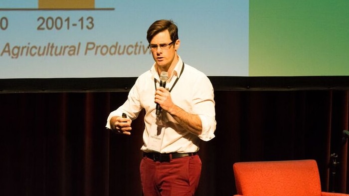 A man stands on a stage and speaks into a microphone.