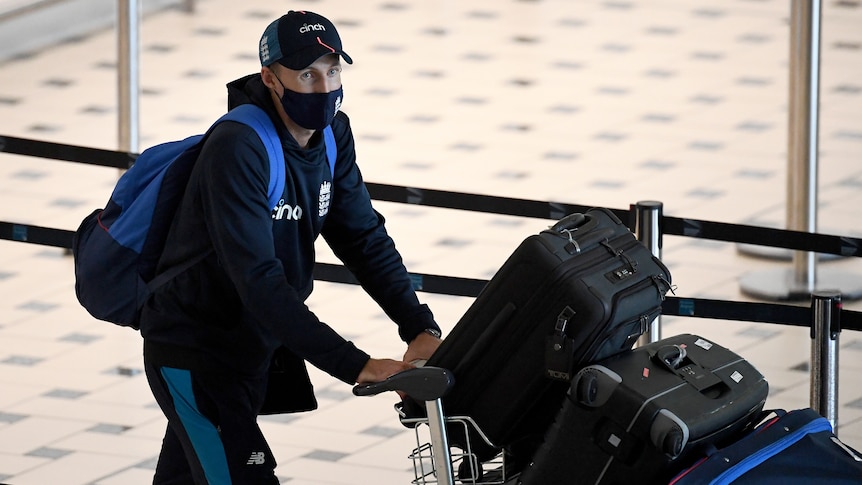 A mask and cap-wearing English cricketer pushes a luggage trolley through arrivals hall of Brisbane Airport ahead of the Ashes. 