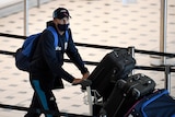 A mask and cap-wearing English cricketer pushes a luggage trolley through arrivals hall of Brisbane Airport ahead of the Ashes. 