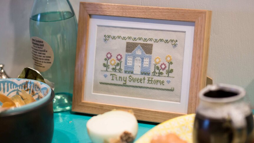 An embroidered picture saying 'Tiny Sweet Home' sits on the bench.