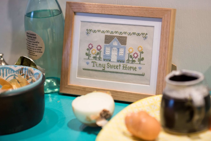 An embroidered picture saying 'Tiny Sweet Home' sits on the bench.