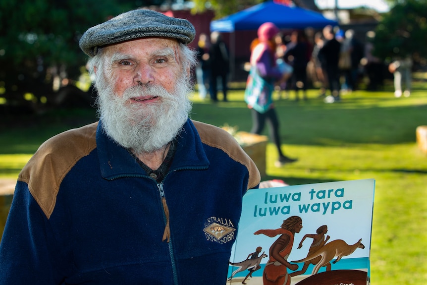 An elderly man holds the book luwa tara luwa waypa