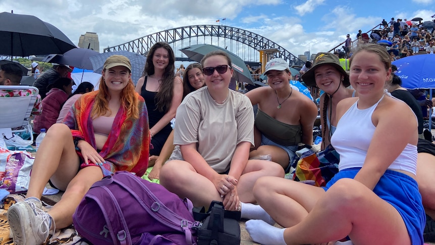 a group of young women siting outdoors on the sydney opera house forecourt 