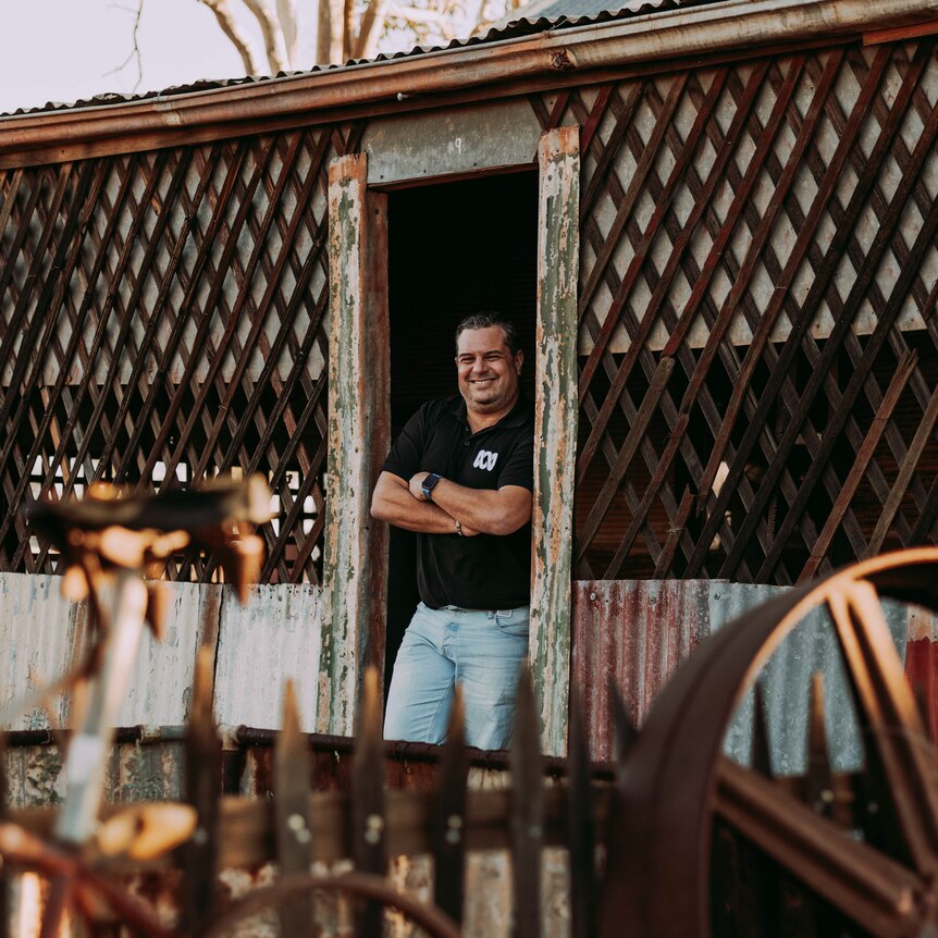 Ivo Da Silva leaning in the doorway of a rusty hut, in the middle of a junkyard full of rusty bikes and wheels.