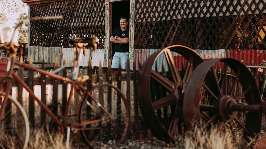 Ivo Da Silva leaning in the doorway of a rusty hut, in the middle of a junkyard full of rusty bikes and wheels.