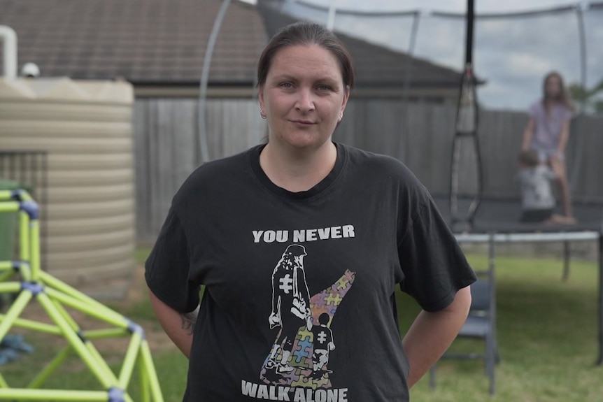A woman stands outside her home while children jump on trampoline.