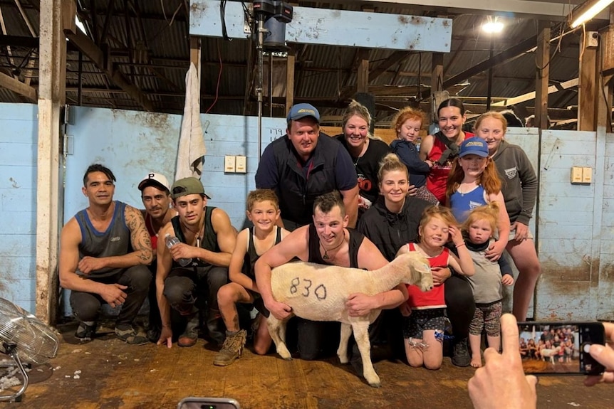 A large group of people pose with a lamb for a photo