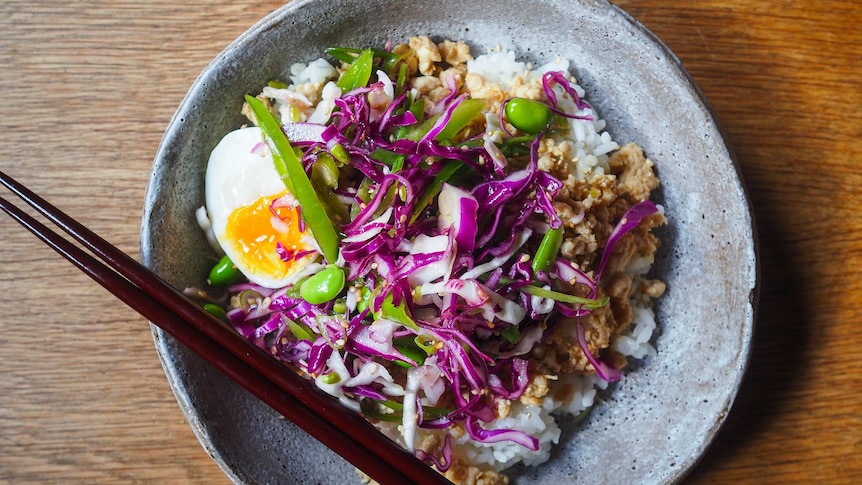 A bowl of rice topped with minced chicken, half an egg and cabbage slaw with edamame, a quick weeknight dinner.