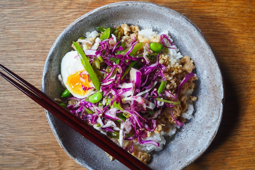 A bowl of rice topped with minced chicken, half an egg and cabbage slaw with edamame, a quick weeknight dinner.