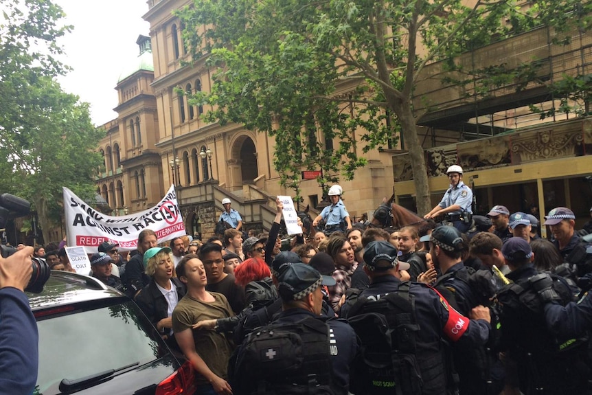 A line of anti-racism and anti-Reclaim Australia protesters push against a row of police, several of whom are mounted on horses.