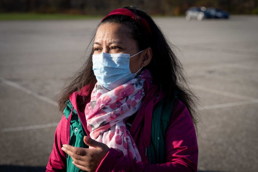 A woman in a mask and a pink scarf and jacket looks concerned
