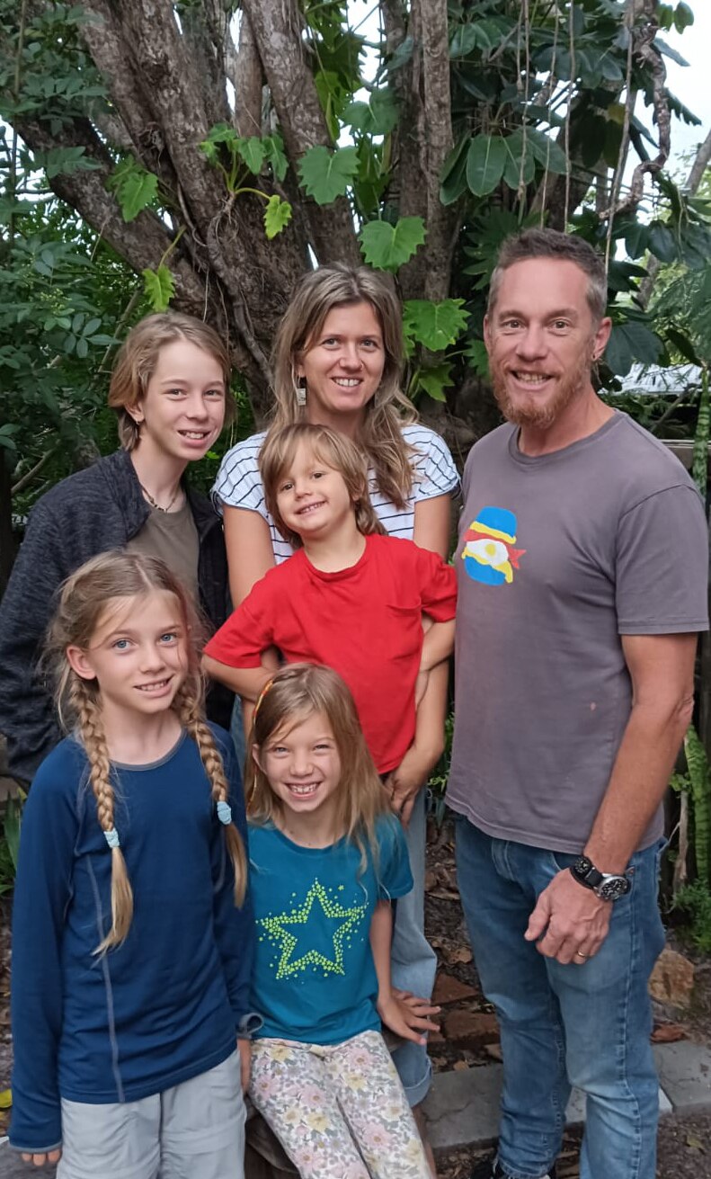 A mother and father with their children, two girls and two boys, standing in the garden smiling at the camera. 