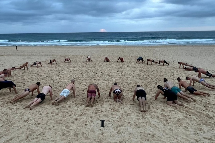 24 men form a circle with their hands and feet on the ground in a push up position
