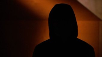 A dark picture of a person wearing a hood in silhouette.
