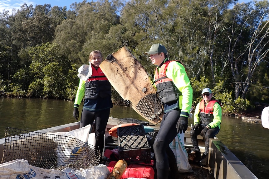 Two students from Kincumber High stand on a boat holding rubbish found in local waterways.