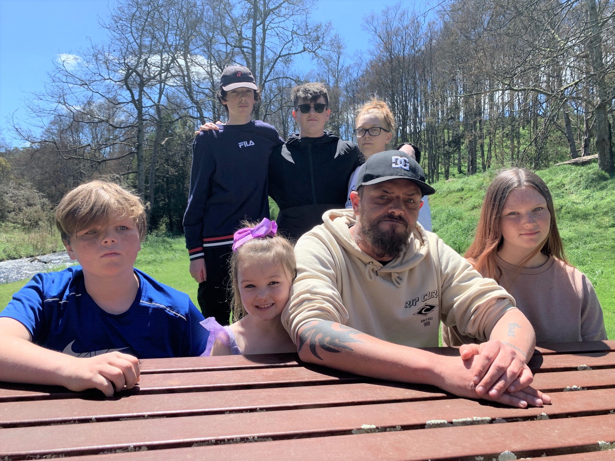 A man sits at a picnic table with a number of children.