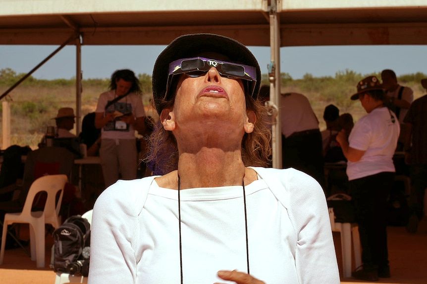 A lady is wearing solar ecclipse glasses looking in awe at the sky above