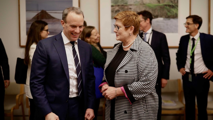 Dominic Raab and Marise Payne talk across a table surrounded by staffers and media.