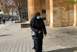 A woman wearing a hijab and a face mask walking outside a court building