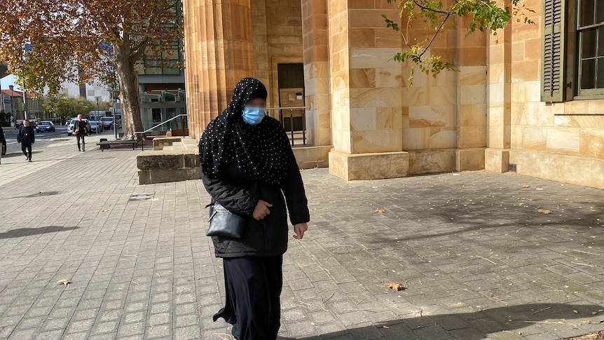 A woman wearing a hijab and a face mask walking outside a court building