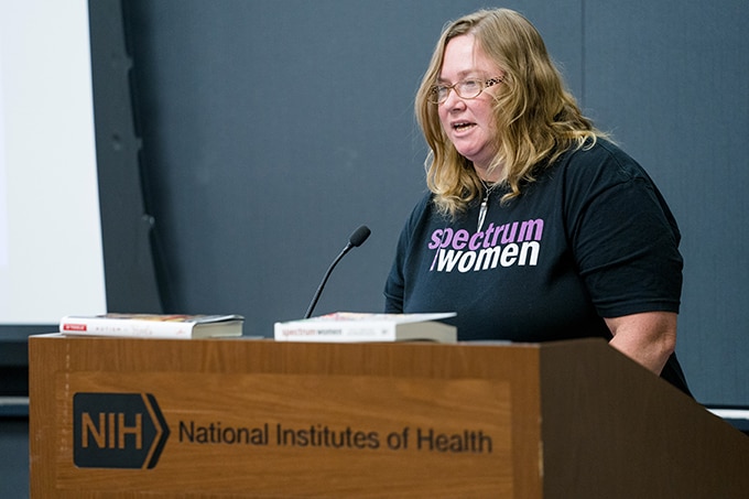 Woman in t-shirt with Spectrum Women branding speaking at a lectern.
