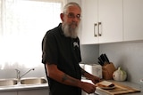 A man standing in a kitchen making a sandwich. 