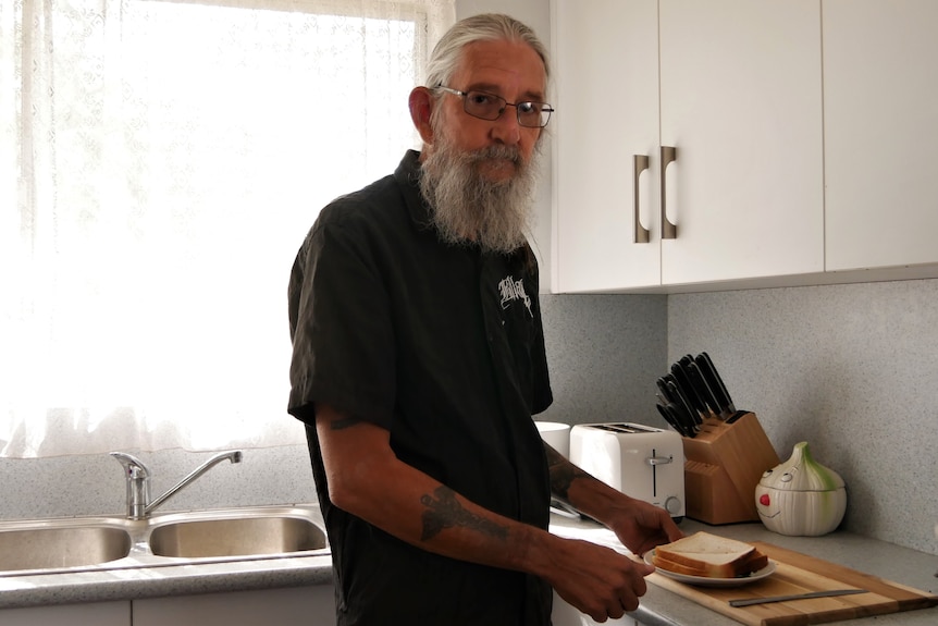 A man standing in a kitchen making a sandwich. 