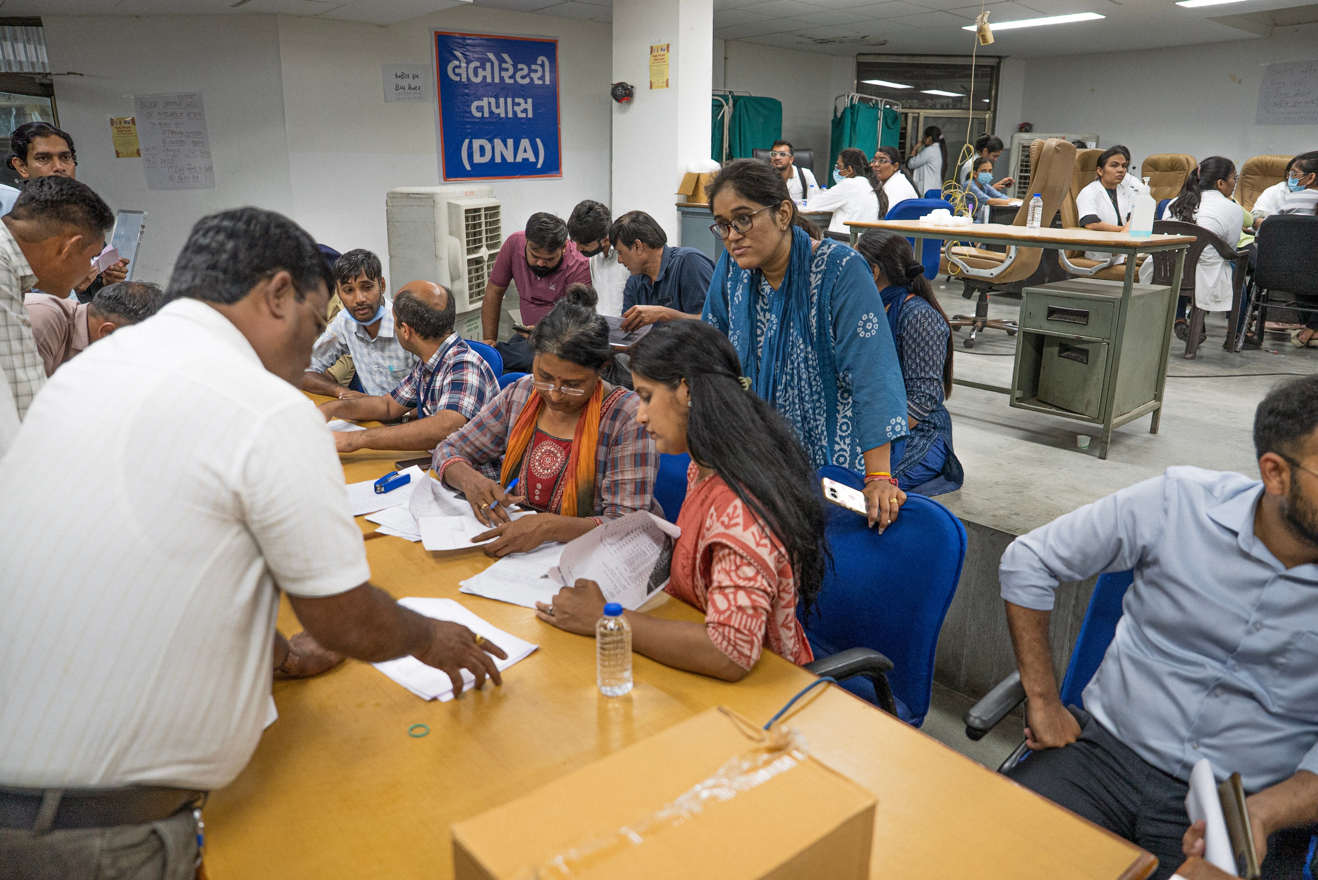Indian residents sitting at desks looking at paperwork inside a DNA centre.