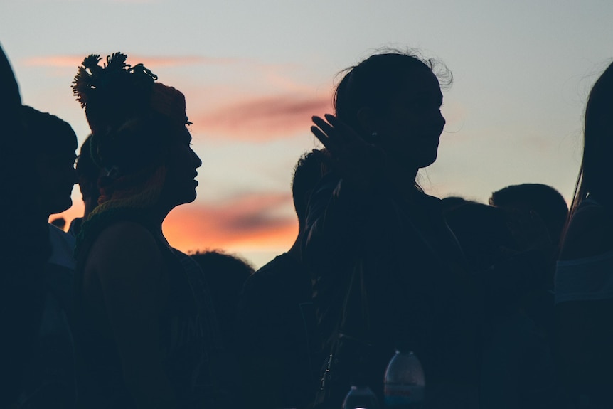 Under a pink night sky, there are silhouetted images of a group of young people standing.