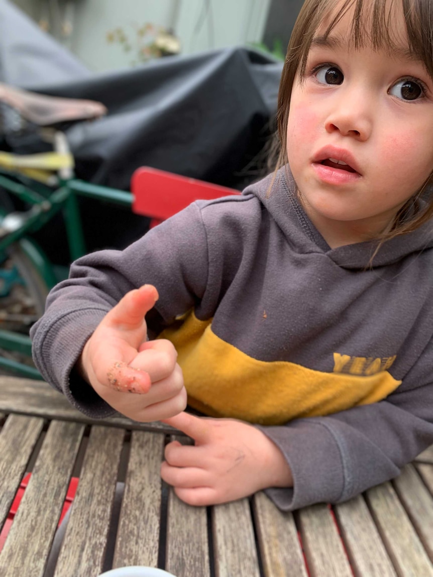 A young girl points to her finger, which is covered in pepper and soap.