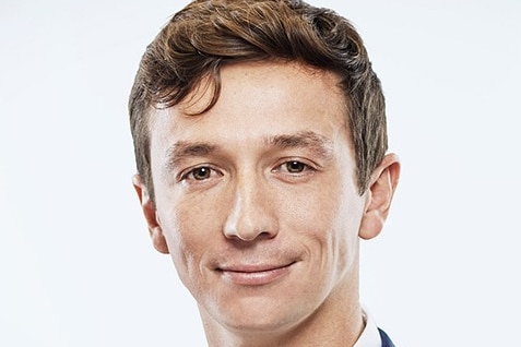 Mitch East smiling wearing a navy suit and white shirt against a white background