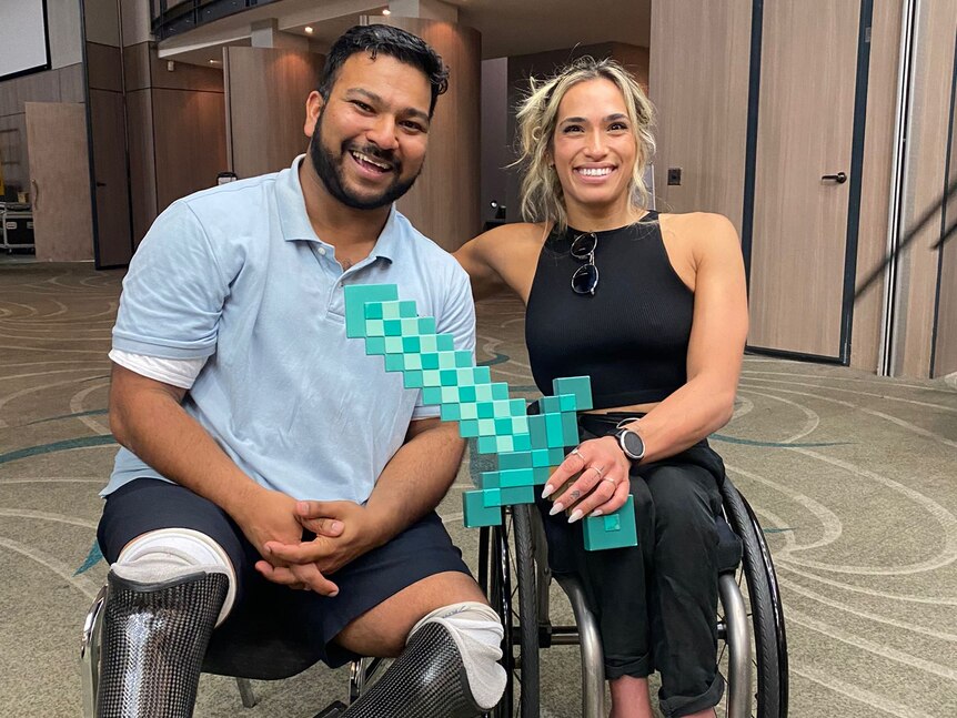 Dwayne Fernandes, a double leg amputee, sits next to wheelchair racer Madi de Rozario, who holds a Minecraft sword.
