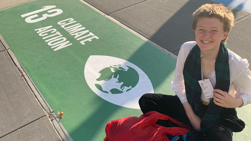 Harriet O'Shea Carre sits next to a sign that reads 'climate change'.
