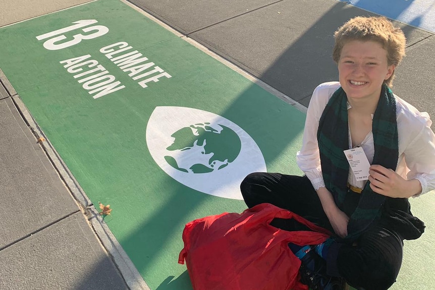 Harriet O'Shea Carre sits next to a sign that reads 'climate change'.