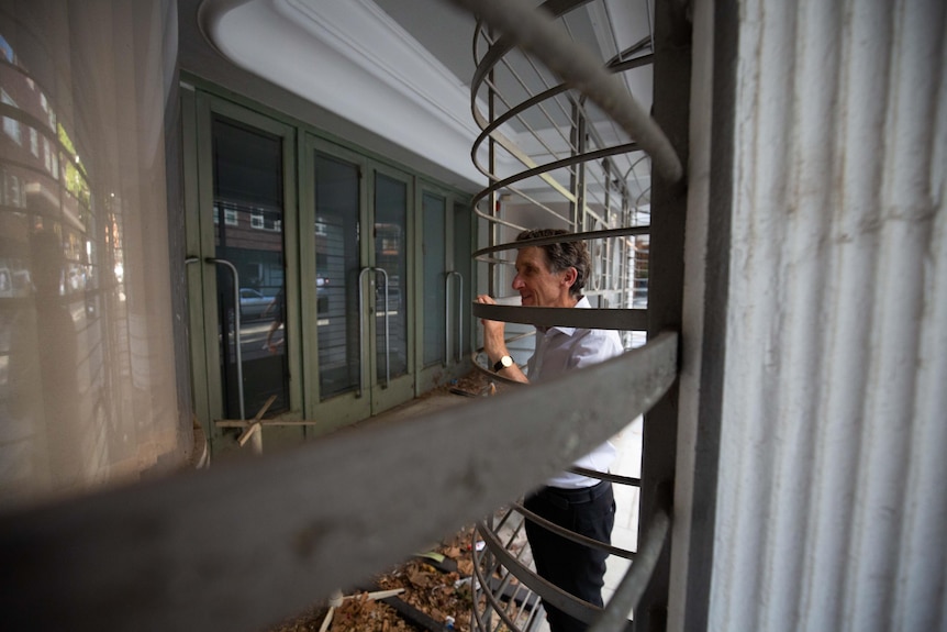 A middle-aged man looks through a metal gate at a window and doors