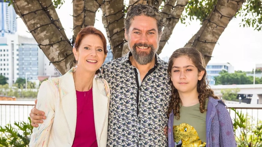 A man stands with his arms around a woman and a young boy, they're all smiling