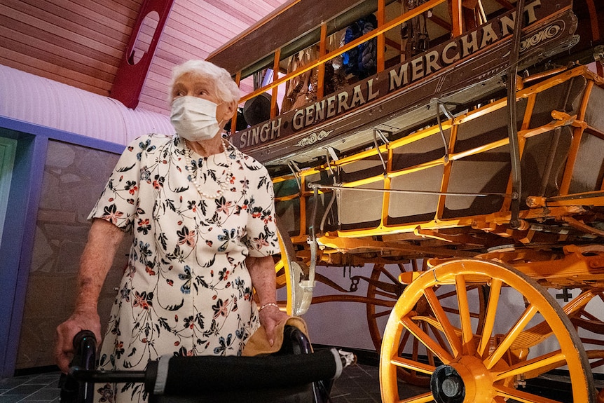 Amy Crosbie, stands with a face mask on, next to a wooden coach.