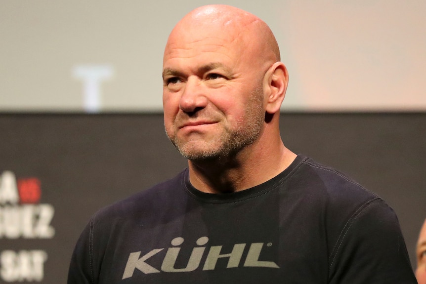 A bald man wearing a black t-shirt smirks. 