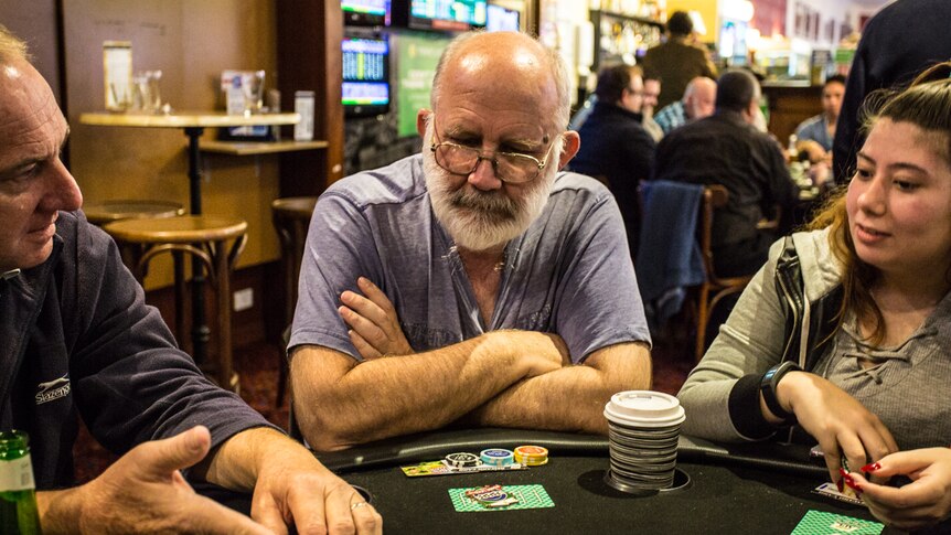 Centrelink worker Jim perfecting his poker face whilst sitting at a table, flanked by two other players.