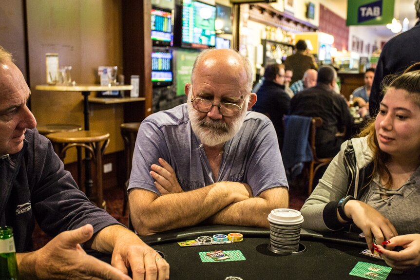 Centrelink worker Jim perfecting his poker face whilst sitting at a table, flanked by two other players.
