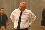 Scott Morrison stands in front of fire-ravaged bushland with a serious expression on his face.