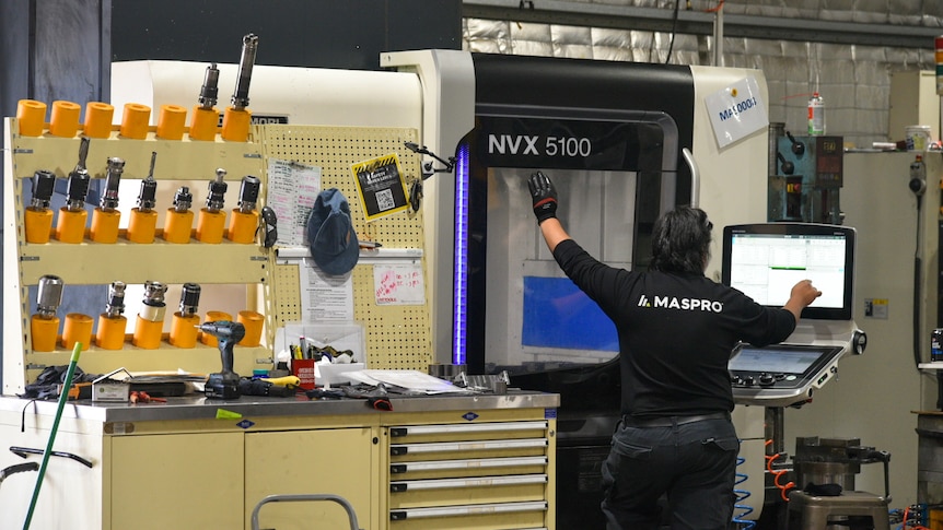 A man stands in front of a large box-shaped machine with a glass door and small laptop attached.