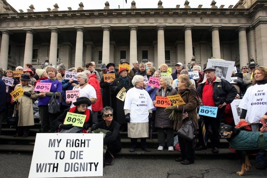 Protesters hold signs on the steps of Victorian Parliament as they lobby for assisted-dying to be legal.